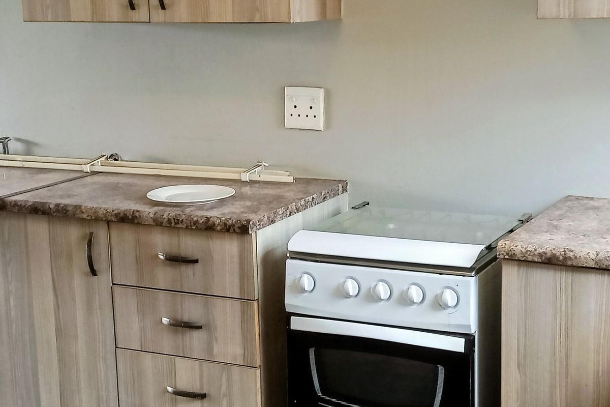 A functional kitchen area featuring light wood-grain cabinetry, laminate countertops, and a freestanding stove.