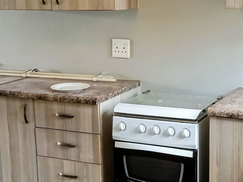 A functional kitchen area featuring light wood-grain cabinetry, laminate countertops, and a freestanding stove.