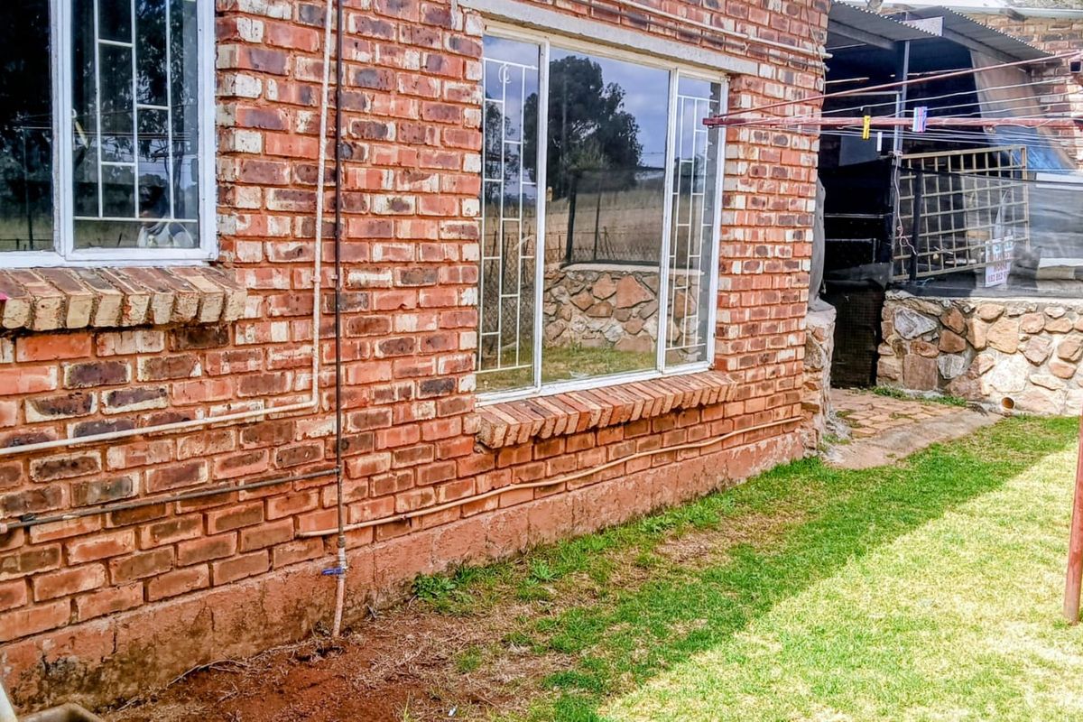 Rear exterior view of the house featuring exposed brick walls, security window bars, and a stone retaining wall in the garden area.