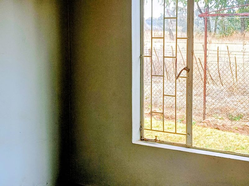 An empty room featuring a sliding window with security bars, overlooking an outdoor area.