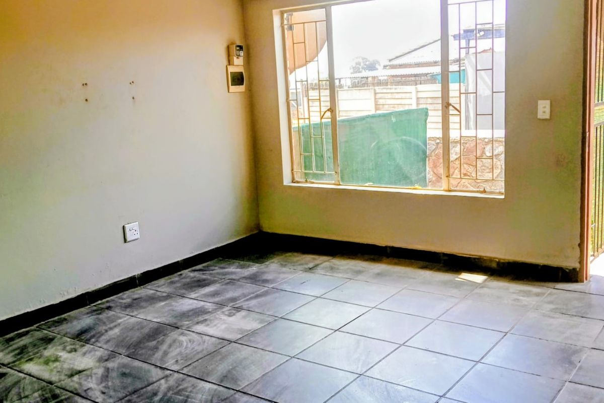 An empty living room featuring tiled flooring, security bars on the window, and neutral walls, offering a blank canvas for potential renovation.