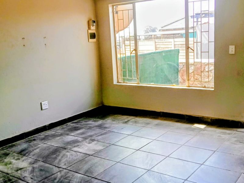 An empty living room featuring tiled flooring, security bars on the window, and neutral walls, offering a blank canvas for potential renovation.