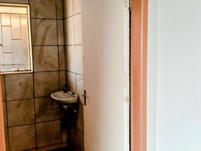 A small, dated bathroom featuring tiled walls and a wall-mounted basin, requiring significant cosmetic updates and maintenance.