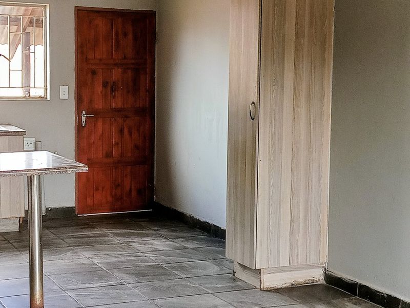 A functional kitchen area featuring tiled floors, built-in cabinetry, a sink, and a wooden door, offering a blank canvas for potential updates.