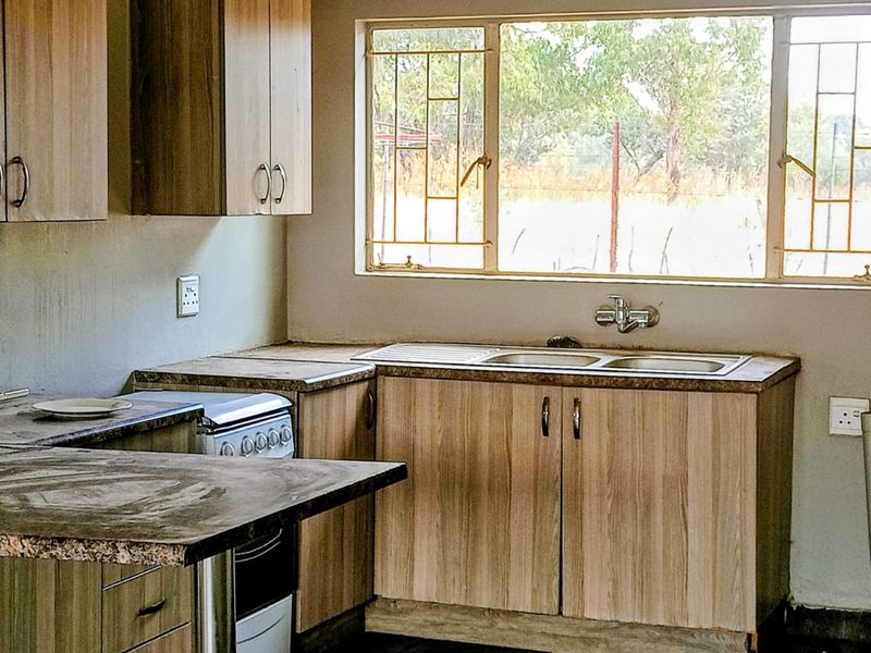 A functional kitchen featuring wood-look laminate cabinetry, laminate countertops, a stainless steel sink, and a freestanding stove, with security bars on the window.