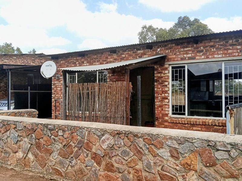 Front view of a single-story house featuring exposed brick construction, a corrugated metal roof, and a stone boundary wall.