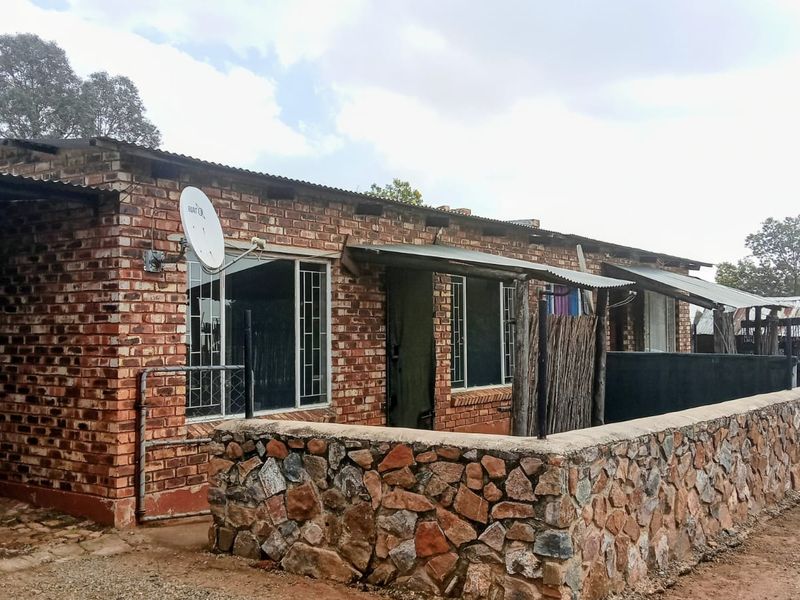 A single-story house featuring an exposed brick exterior, a stone masonry boundary wall, and a corrugated metal roof with security-barred windows.