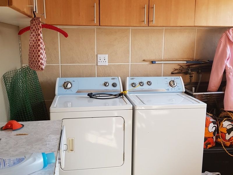 A functional laundry room featuring built-in wooden cabinetry, tiled splashbacks, and tiled flooring with space for a washing machine and dryer.