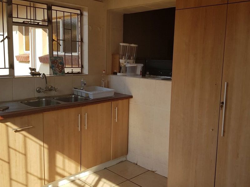 A functional scullery area featuring laminate cabinetry, a double sink, tiled flooring, and a tall pantry cupboard, providing ample storage and prep space.