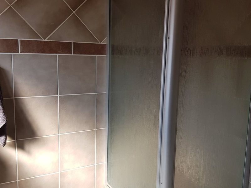 A bathroom featuring a corner shower enclosure with tiled walls and flooring, presenting a functional space ready for potential cosmetic updates.