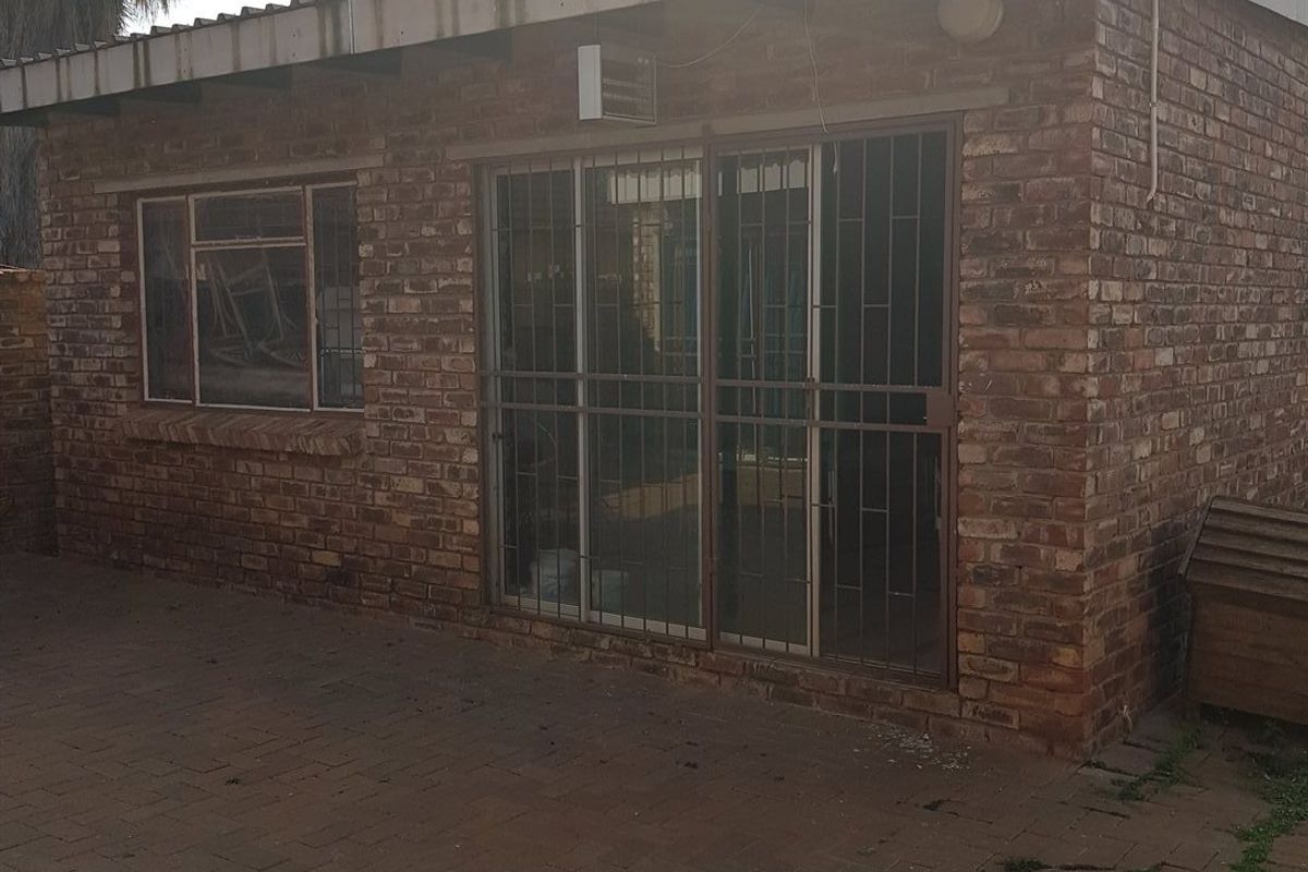 Rear exterior view of a face brick house featuring a paved patio area, sliding glass doors with security gates, and a corrugated roof.