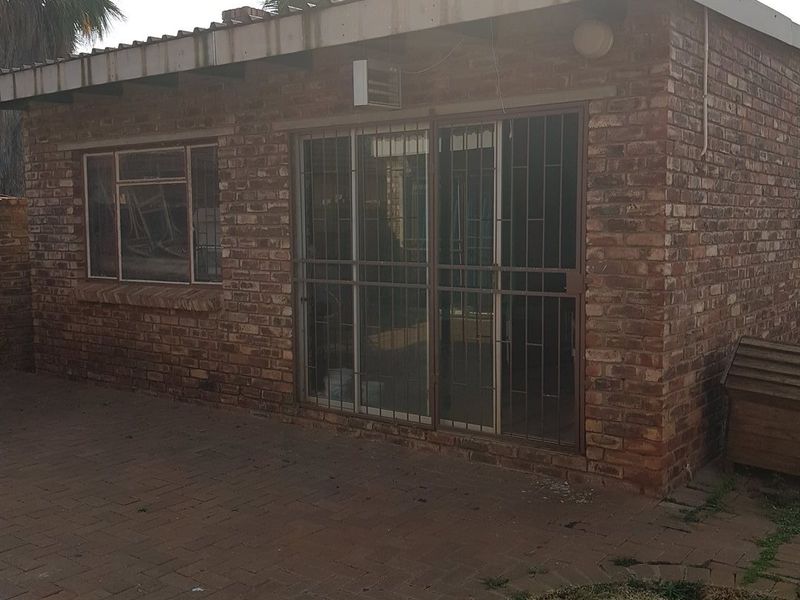 Rear exterior view of a face brick house featuring a paved patio area, sliding glass doors with security gates, and a corrugated roof.