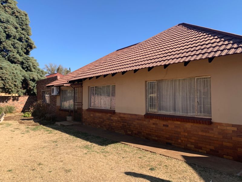 Rear view of a single-story house featuring a tiled roof, brick and plaster facade, and security bars on the windows.