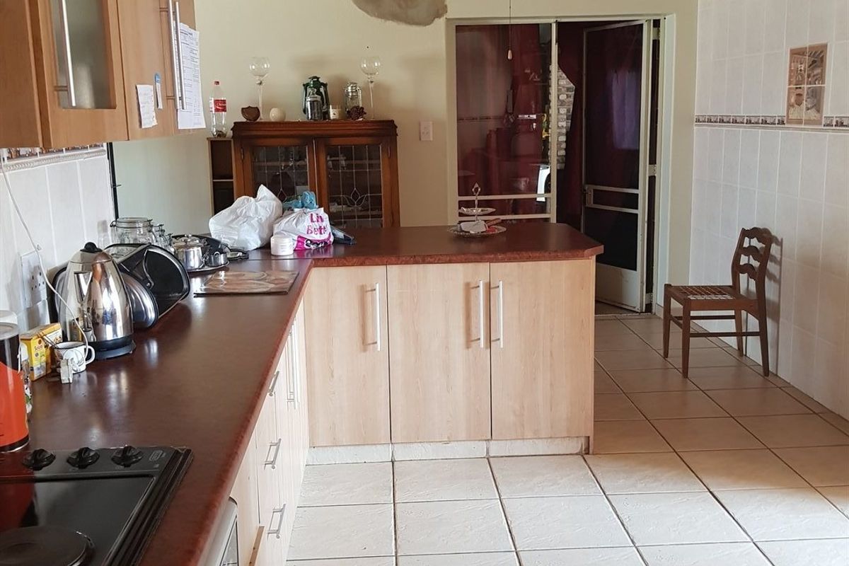 Kitchen featuring light wood cabinetry, dark laminate countertops, tiled flooring, and a timber ceiling, with visible wall damage requiring repair.