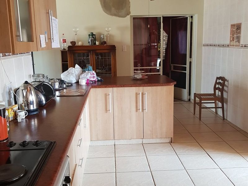 Kitchen featuring light wood cabinetry, dark laminate countertops, tiled flooring, and a timber ceiling, with visible wall damage requiring repair.