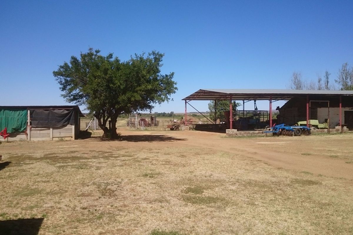 A view of the farm yard featuring an open-sided barn structure and auxiliary outbuildings set within a rural landscape.