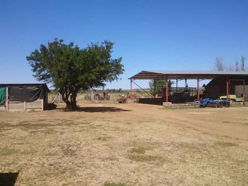 A view of the farm yard featuring an open-sided barn structure and auxiliary outbuildings set within a rural landscape.