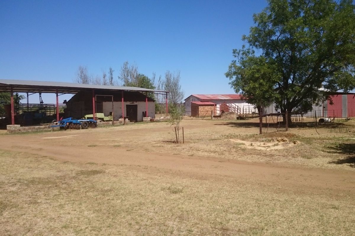 A view of the farm yard featuring multiple outbuildings, a large open-sided steel structure, and surrounding dirt grounds.