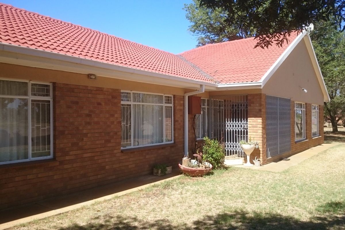 A view of the rear brick facade of the farmhouse, featuring a tiled roof, security gates, and aluminium window frames.