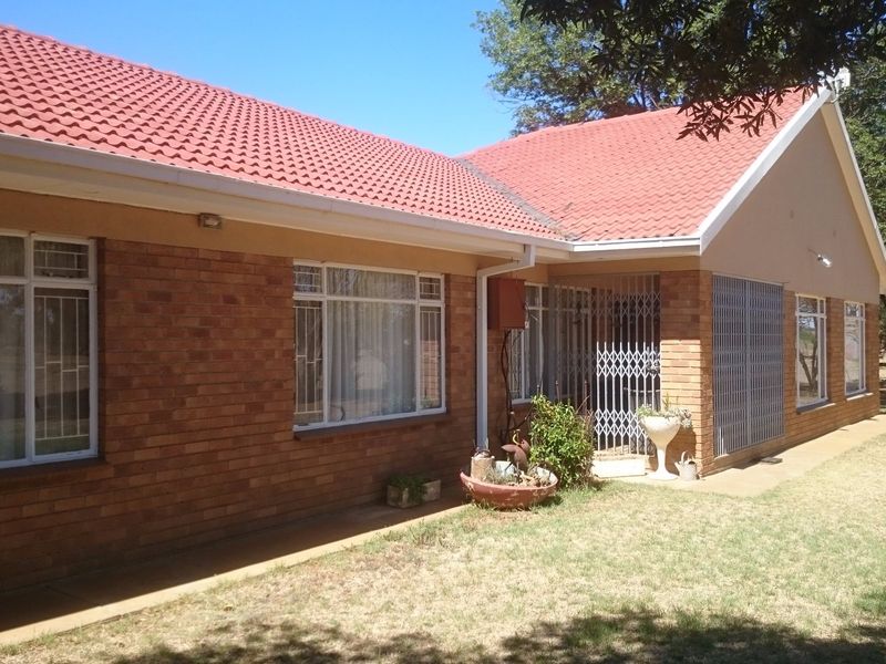 A view of the rear brick facade of the farmhouse, featuring a tiled roof, security gates, and aluminium window frames.