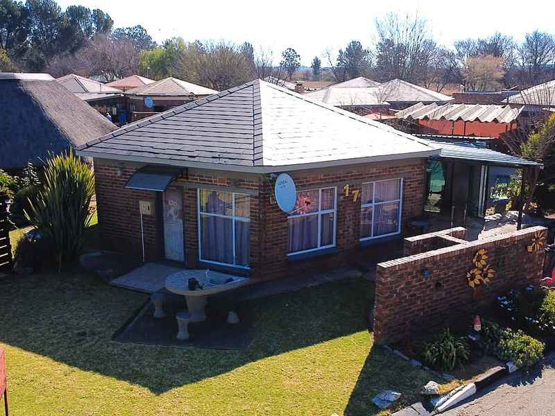 An elevated view of a single-story brick house featuring a hipped roof, aluminum windows, and a front garden with a brick boundary wall.