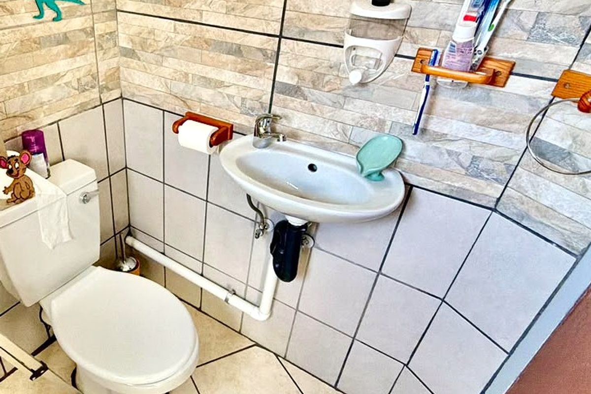 A compact bathroom featuring a wall-mounted basin, standard toilet, and decorative tiled wall finishes.