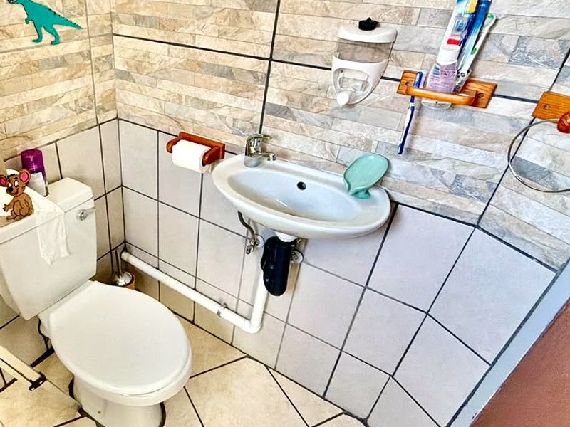 A compact bathroom featuring a wall-mounted basin, standard toilet, and decorative tiled wall finishes.