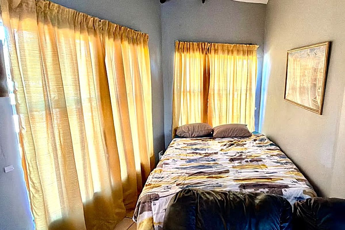 A bedroom featuring tiled flooring and exposed ceiling beams, with natural light entering through large windows.