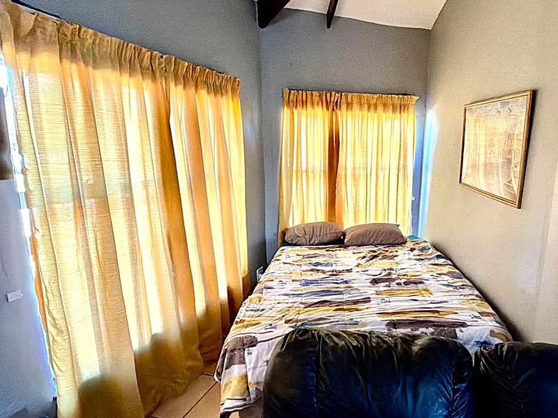 A bedroom featuring tiled flooring and exposed ceiling beams, with natural light entering through large windows.