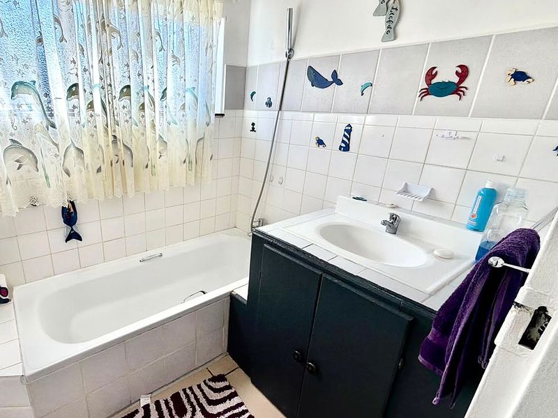 A functional bathroom featuring a built-in bathtub, a vanity cabinet with an integrated sink, and tiled wall finishes.