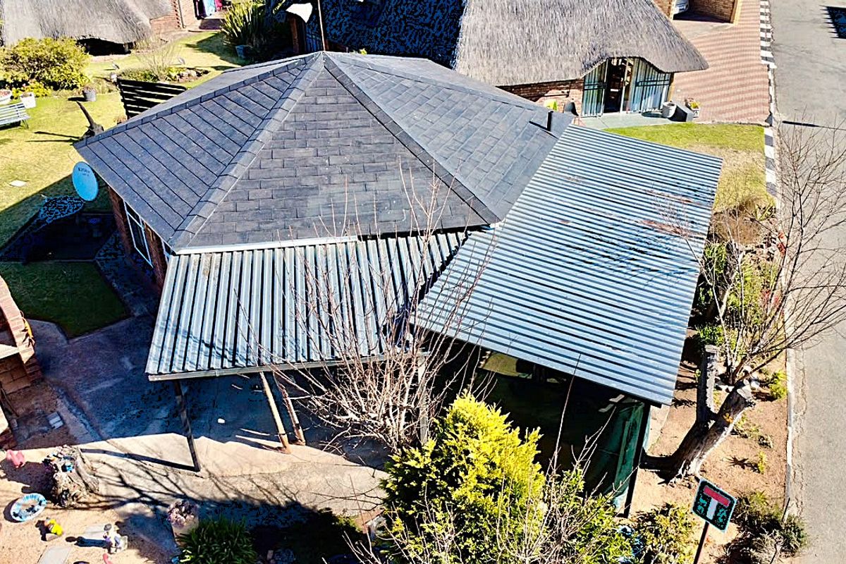 Aerial view of the property showing the roof structure, including a tiled section and a corrugated metal roof over the patio area.