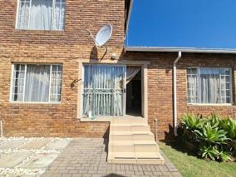Rear exterior view of the townhouse featuring a face brick facade, paved patio area, and concrete steps leading to a sliding glass door entrance.