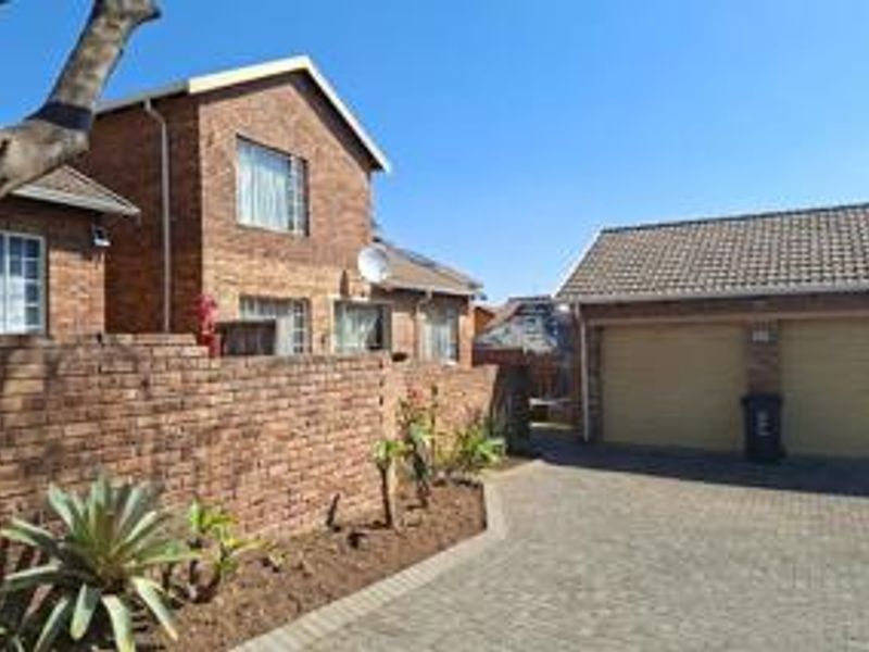 Front view of a face brick townhouse featuring a double garage, paved driveway, and established boundary wall.