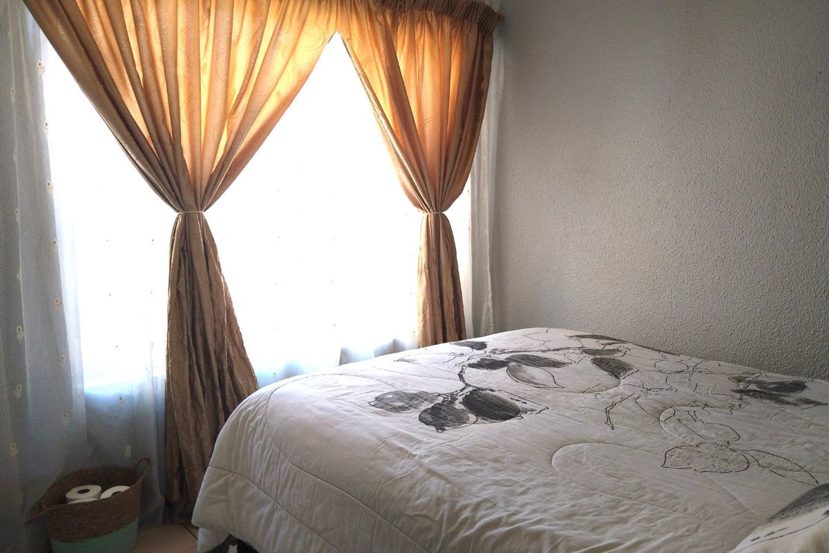A bedroom featuring textured walls and tiled flooring, illuminated by natural light through a window with curtains.