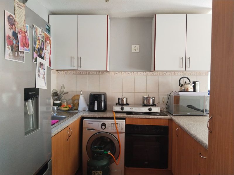 Compact kitchen featuring white upper cabinetry, wood-finish lower cabinets, tiled backsplash, built-in oven, gas hob, and integrated laundry plumbing.