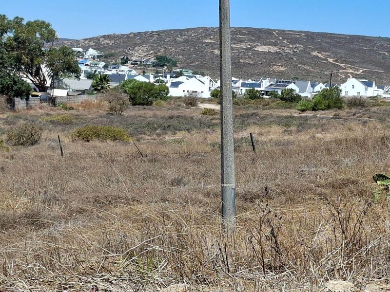 A vacant residential plot featuring natural vegetation and a utility pole, with surrounding neighborhood homes visible in the background.