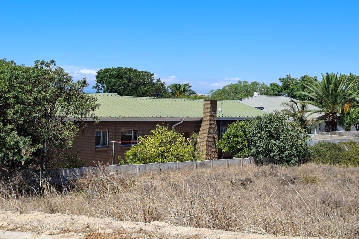 View of the rear elevation of a brick residential property featuring a corrugated metal roof and a brick chimney, set behind a boundary wall.