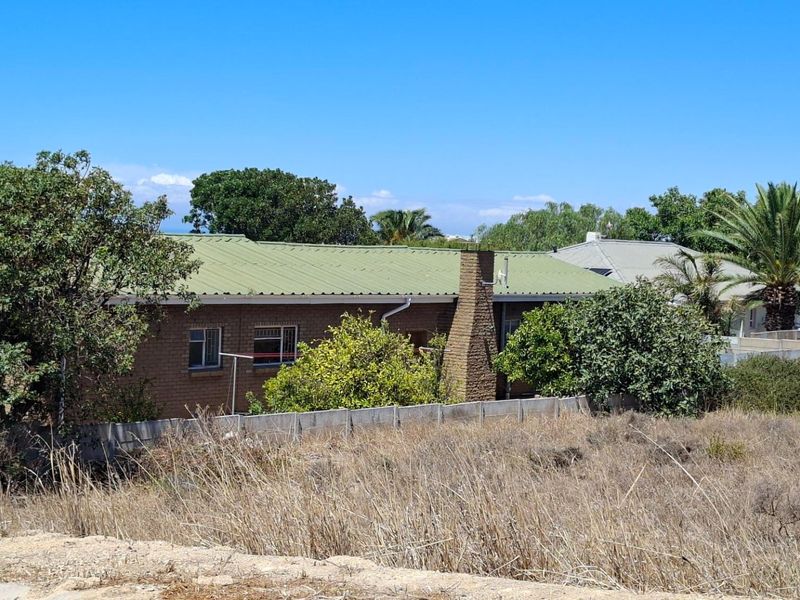 View of the rear elevation of a brick residential property featuring a corrugated metal roof and a brick chimney, set behind a boundary wall.