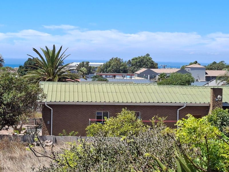 An elevated view overlooking a residential property with a green metal roof, brick exterior, and distant ocean horizon.