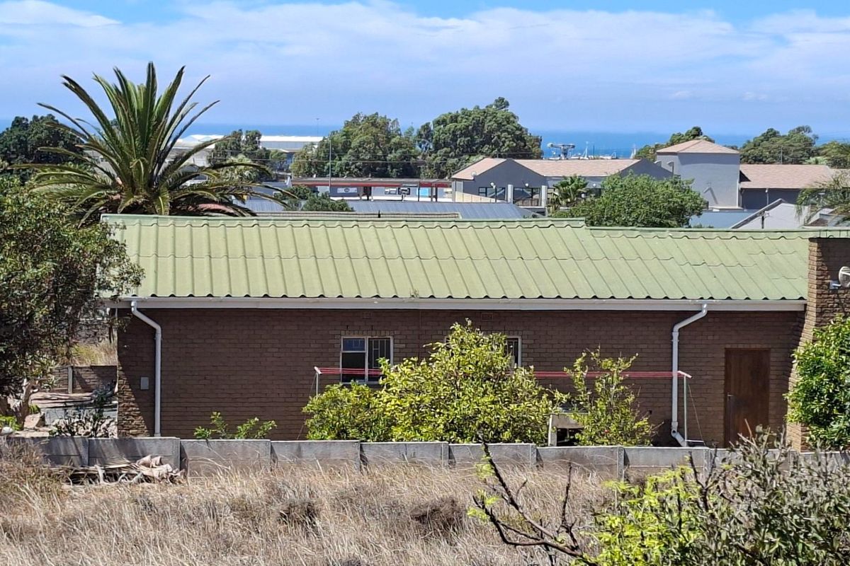 Rear view of a residential property featuring a brick facade, corrugated metal roof, and a precast concrete boundary wall.