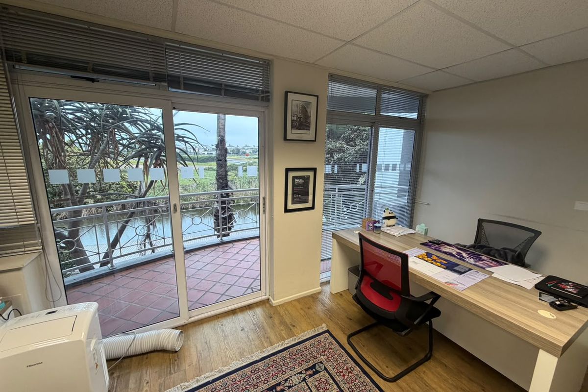 A bright office space featuring laminate flooring, a suspended ceiling, and large sliding glass doors providing access to a private balcony with scenic views.