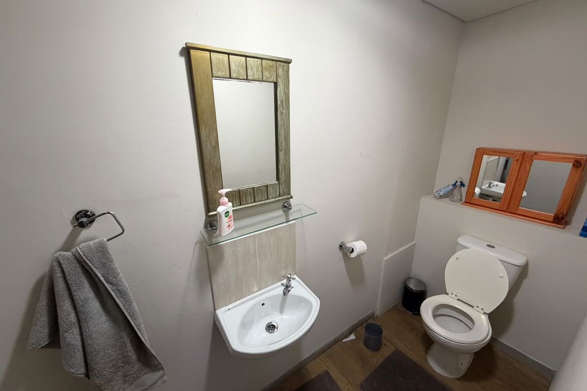 A functional commercial bathroom featuring a wall-mounted basin, toilet, and vanity mirrors.