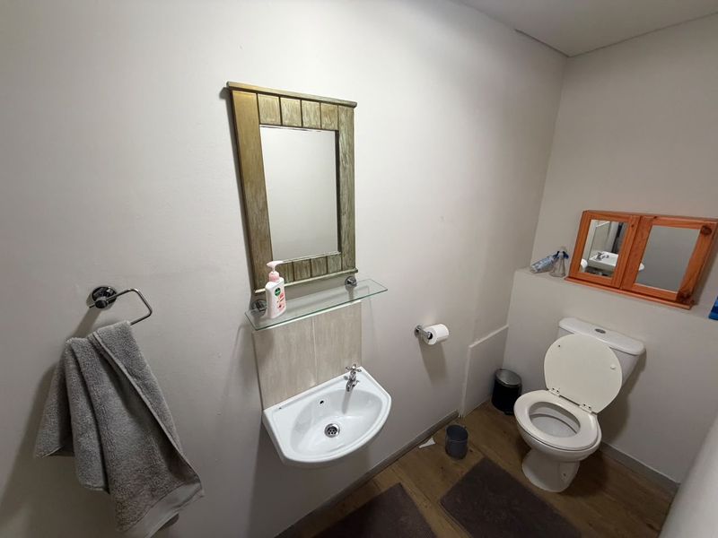 A functional commercial bathroom featuring a wall-mounted basin, toilet, and vanity mirrors.