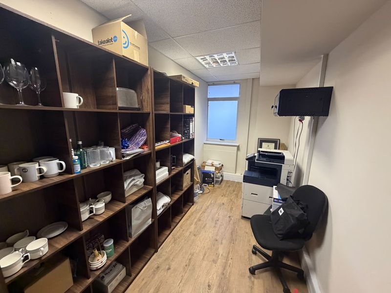 A functional office space featuring built-in dark wood shelving, laminate flooring, and a suspended ceiling with recessed lighting.