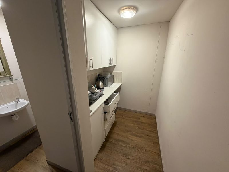A compact scullery area featuring built-in white cabinetry, laminate flooring, and an adjacent small washroom with a wall-mounted basin.