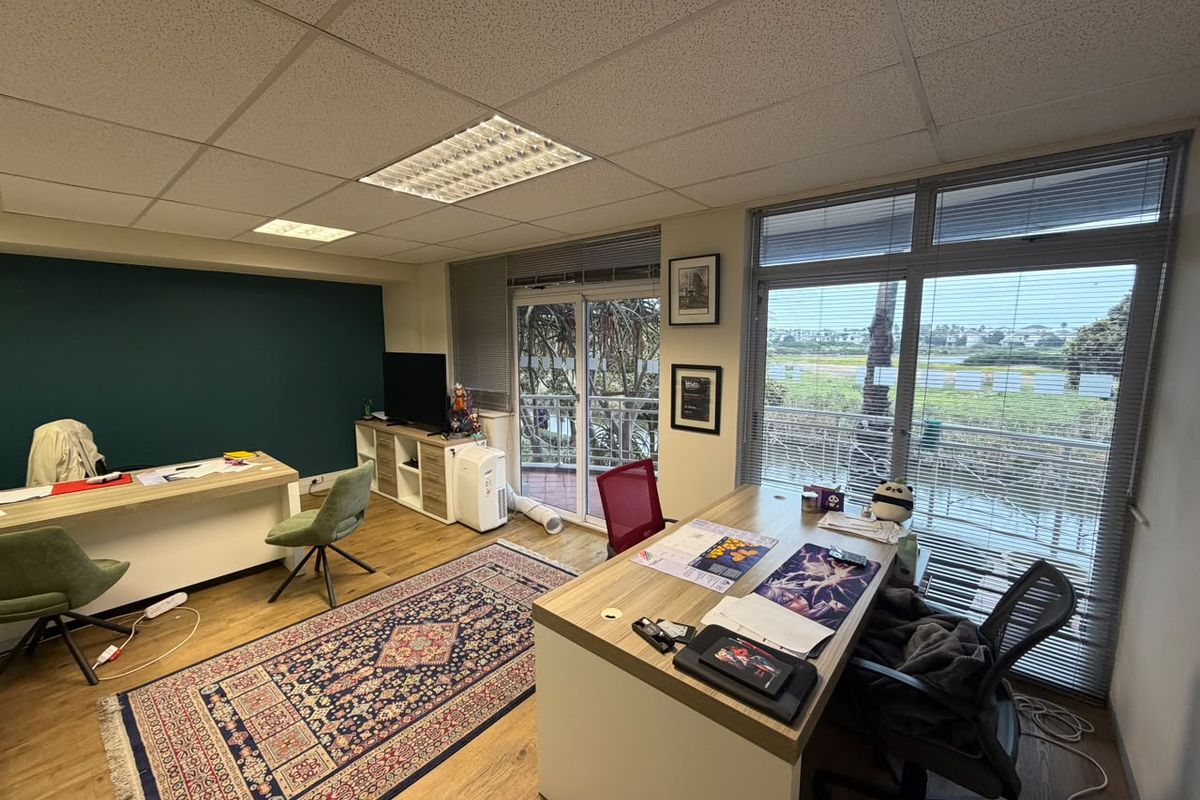 A bright office space featuring laminate flooring, suspended ceilings with recessed lighting, and large windows providing natural light and exterior views.