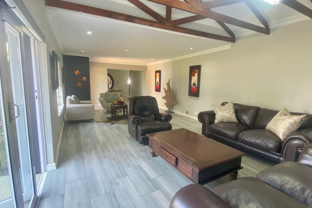 Spacious living room featuring exposed timber roof trusses, wood-look tile flooring, and large sliding glass doors providing natural light.