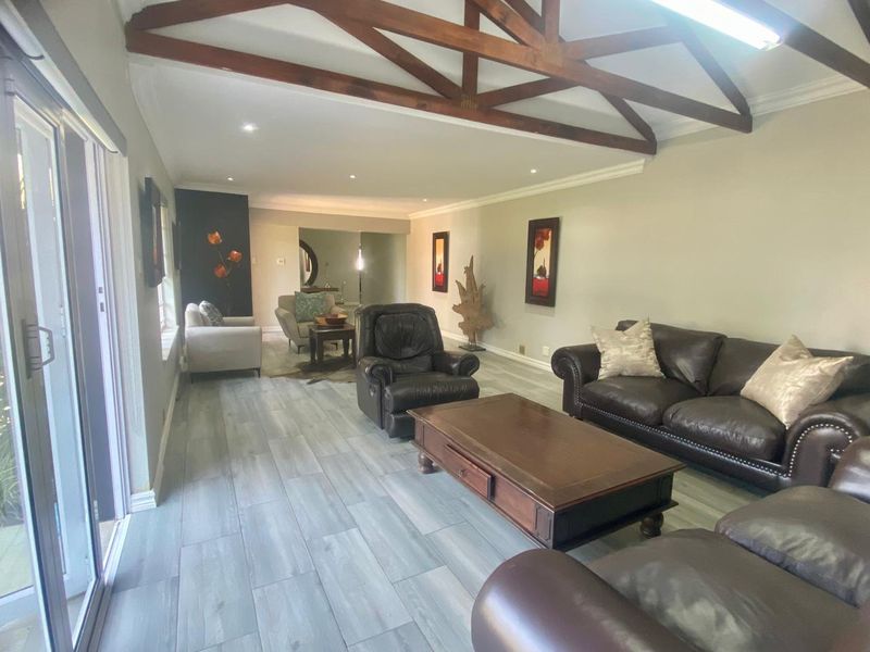 Spacious living room featuring exposed timber roof trusses, wood-look tile flooring, and large sliding glass doors providing natural light.