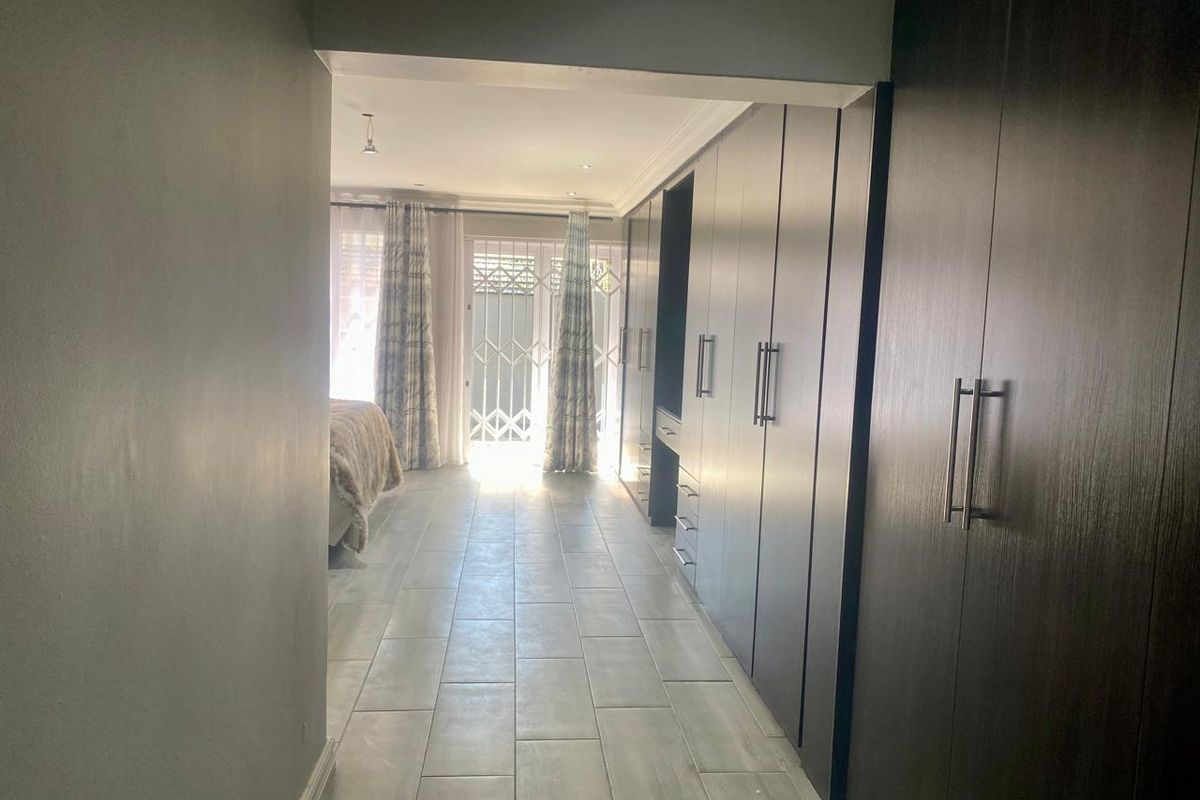 Spacious bedroom featuring extensive dark wood built-in cupboards, modern tiled flooring, and direct access to an outdoor area through a secure gate.