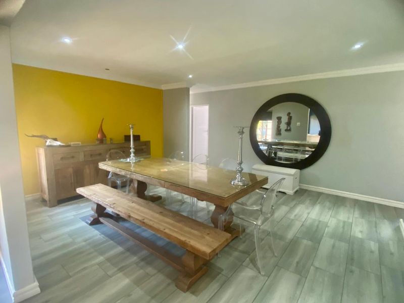 Spacious dining room featuring modern tiled flooring, recessed downlighting, and a bold yellow accent wall, creating a bright and contemporary atmosphere.